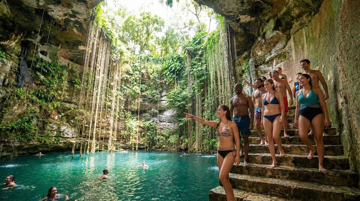 Visitantes bajando la escalera de piedra hacia el agua del Cenote Ik Kil
