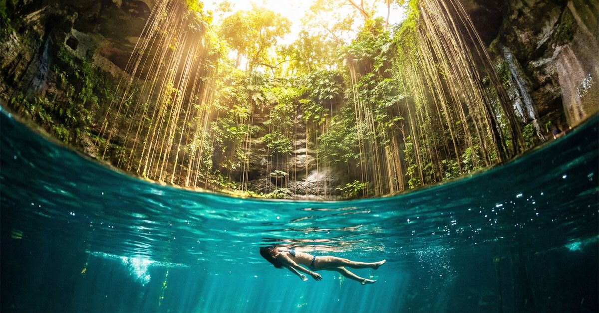 Nadador bajo la superficie del Cenote Ik Kil con rayos de luz